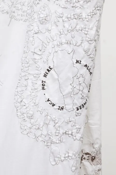 Detail of bedsheet embroidered with human hair. Belonging to the work Migran-t, the embroidery shows the map of Argentina next to the United Kingdom map with the legend "Nor here, not there" in English and Spanish.